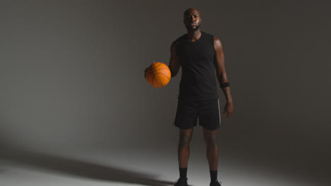 Studioporträt-In-Voller-Länge-Eines-Männlichen-Basketballspielers,-Der-Vor-Dunklem-Hintergrund-Einen-Ball-Dribbelt